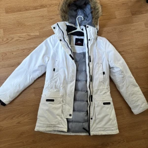 Vit vinterjacka från McKinley - Säljer en snygg och varm vit vinterjacka från McKinley. Jackan har en avtagbar huva med fuskpäls och praktiska fickor med dragkedja. Perfekt för kalla vinterdagar! Den är i bra skick och redo för nya äventyr. 🏔️