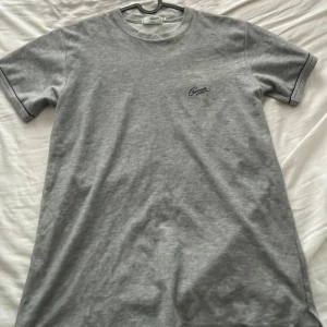 Grå t-shirt från Crocodile - Säljer en stilren grå t-shirt från Crocodile i storlek M. Den är gjord av mjukt bomullsmaterial och har en liten logga på bröstet. Perfekt för en avslappnad vardagslook!