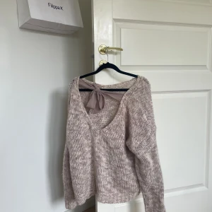 Beige stickad tröja från Cream - Säljer en supermysig beige stickad tröja från Cream. Den har en v-ringad design med en söt rosett i ryggen. Perfekt för höst och vinter när du vill hålla dig varm och stilren. Tröjan har långa ärmar och en lös passform som gör den extra bekväm. Passar perfekt till både jeans och kjol!