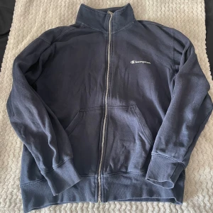 Mörkblå tröja med dragkedja från Champion - Säljer en mörkblå tröja med dragkedja från Champion. Den har en hög krage och två fickor framtill. Tröjan är i bra skick. Kontakta mig om du har fler frågor 😊