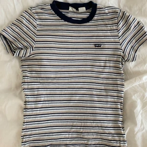 Randig Tshirt - Blå/beige/vit randig T-shirt med Levis-tryck på bröstet. Väldigt skön i materialet, väldigt bra skick!