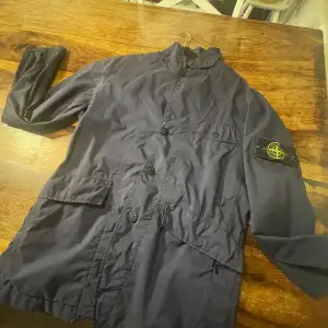 Säljer en snygg mörkblå jacka från Stone Island i mycket bra skick. Jackan har långa ärmar och knappar framtill. Perfekt för höst och vår med sin stilrena design och bekväma passform. Märkeslogga på ärmen ger en extra touch av stil.