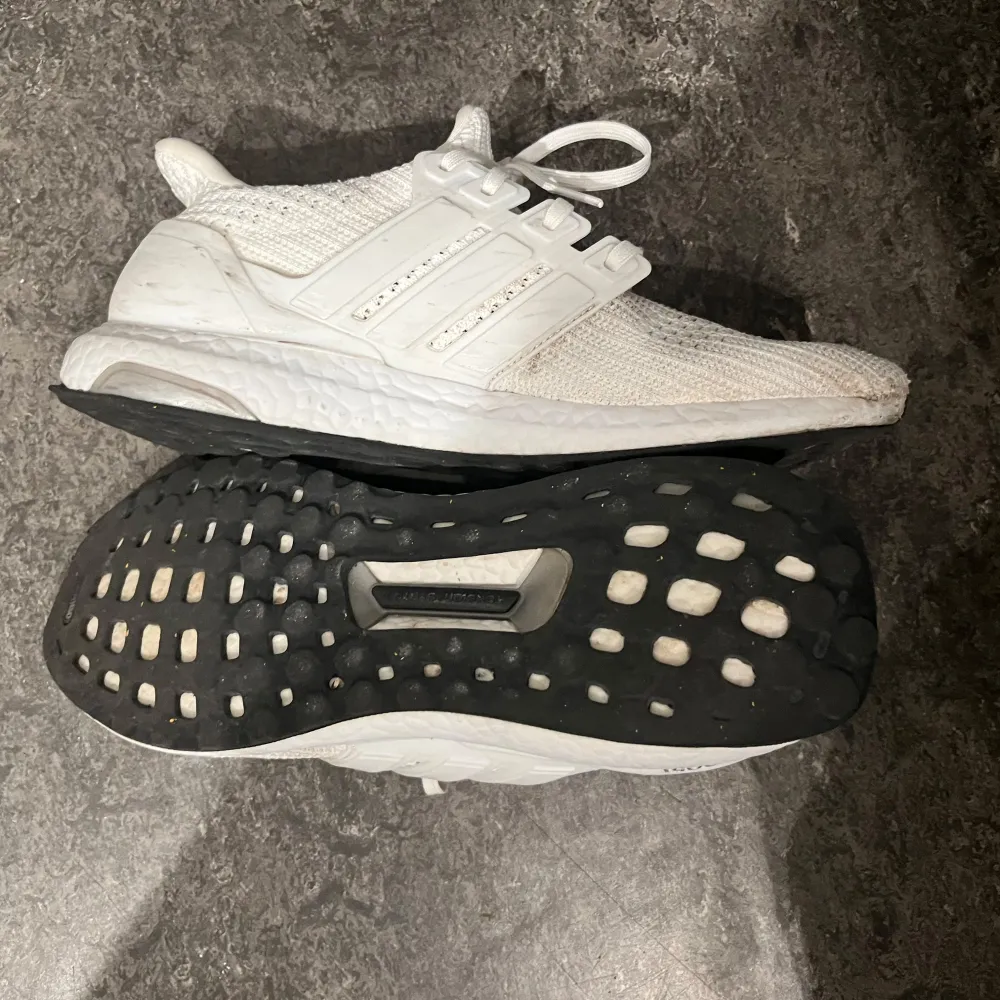 Säljer ett par vita Adidas Ultraboost sneakers i bra skick. De har en snygg och stilren design med stickat material och klassiska tre ränder på sidan. Perfekta för både träning och vardagsbruk. Sulan är svart med vit boost-dämpning för extra komfort. Passar perfekt för dig som vill ha både stil och funktion.. Skor.