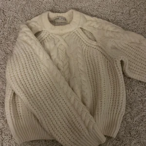 Vit stickad tröja - Mysig vit stickad tröja med flätmönster. Perfekt för kyliga dagar och ger en stilren look. Tröjan har långa ärmar och en rund halsringning. Passar bra till både jeans och kjol.