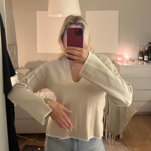 Beige v-ringad tröja - Säljer en superfin beige tröja med v-ringning från NA-KD. Den har vita detaljer som följer längs de långa ärmarna samt vid mudden på tröjan. Använd endast 1 gång. Strl S