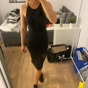 Svart ribbad klänning - Snygg svart ribbad klänning i tight passform. Klänningen är ärmlös och har en stilren design som framhäver figuren. Ett måste i garderoben för alla som älskar stilrena plagg!
