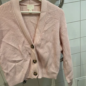 Ljusrosa stickad kofta - Mysig ljusrosa stickad kofta med stora knappar framtill. Perfekt för kyliga dagar och ger en söt touch till din outfit. Koftan har en normal passform och långa ärmar. Ett måste för höstgarderoben! 🍂