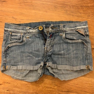 Blå jeansshorts med broderade fickor - Säljer ett par snygga blå jeansshorts i bra skick. Perfekta för sommaren och avslappnade dagar. De är lågmidjade och har en bekväm passform. Storlek står inte men skulle säga 34