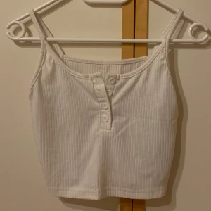 Vitt linne med knappar  - Vitt linne med knappar på framsidan som går att stänga och öppna. Knappt använd så är i fint skick.