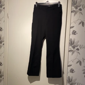 Svarta kostymbyxor från BikBok - Snygga svarta kostymbyxor från BikBok i storlek 38. De har en klassisk design med låg midja och lätt utsvängda ben, perfekt för både jobb och fest. Byxorna är i mycket bra skick och har en stilren look som passar till det mesta. Ett måste i garderoben för en chic och professionell stil!