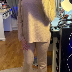 Beige stickad tröja och byxor - Säljer ett supermysigt set med en beige stickad tröja och matchande byxor. Tröjan har en avslappnad passform med långa ärmar och en V hals. Perfekt för höst och vinter när du vill vara både bekväm och stilren. Passar lika bra hemma som ute på stan!