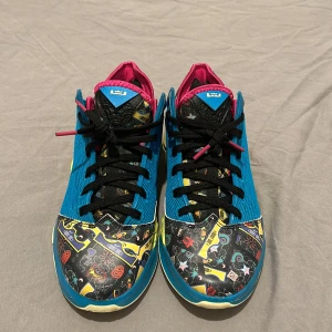 Lebron 19 low  - Säljer ett par unika och färgglada Nike sneakers i mycket bra skick. Skorna har en cool mix av blått, rosa och gult med ett mönster som verkligen sticker ut. Perfekta för att liva upp vilken outfit som helst! De har en bekväm passform och är idealiska för både vardag och träning.
