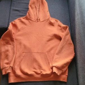 Orange hoodie från H&M - Säljer en orange hoodie från H&M i storlek M. Den har en avslappnad passform och en klassisk känguruficka framtill. Tyvärr finns det ett litet hål vid nederkanten, men annars i bra använt skick. Perfekt för höstmys eller chill dagar. 🧡