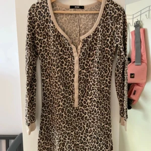 Leopardmönstrad klänning från Bik Bok - Snygg leopardmönstrad jumpsuit från Bik Bok i storlek S. Klänningen har långa ärmar och en v-ringad hals med knappar framtill. Perfekt för en trendig och djärv look. Materialet känns mjukt och bekvämt, idealiskt för både vardag och fest. Men passar stl M/L