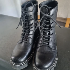 Svarta boots från VC Cobler - Snygga svarta boots i skinn från VC Cobler. De har en robust design med snörning och dragkedja för enkel på- och avtagning. Perfekta för höst och vinter med en slitstark sula som ger bra grepp. Passar både till vardags och lite tuffare outfits.