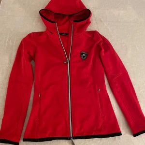 Röd tröja med huva från J.Lindeberg - Säljer en röd tröja från J.Lindeberg i mycket bra skick. Perfekt för höst och vår! Perfekt för skidsäsongen eller träning