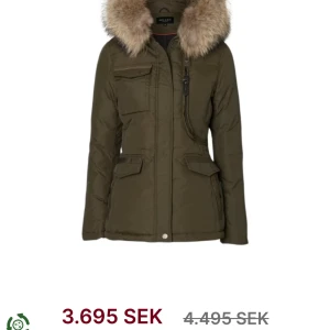 Olivgrön parkajacka med pälsdetaljer - Säljer en snygg olivgrön parkajacka från Hollies. Jackan har en mysig pälsdetalj på huvan och flera praktiska fickor framtill. Perfekt för kyliga höst- och vinterdagar. Den har en dragkedja och knappar för extra skydd mot kylan. Inga defekter