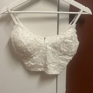 Vit spetslinne med guld dragkedja - Säljer en superfin vit spetslinne med smala axelband och en guld dragkedja i ryggen. Perfekt för sommardagar eller festliga tillfällen. Den har en vacker spetsdesign som ger en romantisk touch. Helt oanvänd🥰