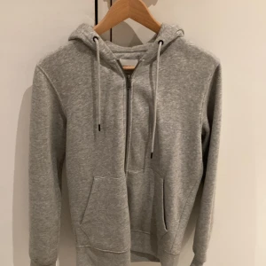 Grå hoodie från Jack & Jones - Säljer en snygg och bekväm grå hoodie från Jack & Jones. Den har en dragkedja framtill och en praktisk känguruficka. Perfekt för både höst och vår, och funkar lika bra till vardags som till träning. Huvan har justerbara snören för extra komfort.