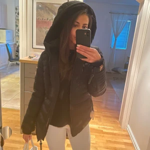 Svart pufferjacka från Marikoo - Vinterjacka köpt från Zalando för 1061kr, märket  Marikoo och är aldrig använd och har inga skador, Storlek M men skulle säga att den är liten i storleken då den sitter bra på mig som bär xs/s. Jackan har ett mjukt fuskpälsfoder och en stor huva för extra värme. Den är perfekt för kalla vinterdagar och har en dragkedja framtill samt praktiska fickor med dragkedjor. Supermysig och stilren!