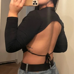 Svart långärmad topp med öppen rygg - Säljer en snygg svart långärmad topp med en öppen rygg och knytning. Perfekt för en utekväll eller fest! Bra skick:)