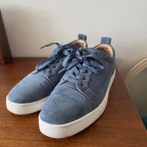 Blå sneakers i mocka - Säljer ett par snygga blå sneakers i mocka med vit sula. Skorna har snörning och en cool röd undersida. Perfekta för både vardag och fest!