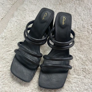 Svarta sandaler från Clarks - Säljer ett par stilrena svarta sandaler från Clarks. De har en fyrkantig tå och flera remmar över foten som ger en modern look. Perfekta för både vardag och fest!