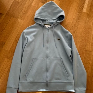 Lacoste zip hoodie babyblå - Säljer nu min väldigt fina samt väldigt sällsynta lacoste zip hoodie då den knappt har använts, det är storlek S på den och skicket är i toppskick.