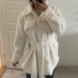 Varm Teddy jacka med band och vita integrerade knappar - En vit/offwihite Teddy jacka med ett brett band och knappar på framsidan samt på ärmen. Fickor vid bröstet. Och en mjuk krage. Nästan oanvänd. Återpublicerar en tidigare annons då jag verkligen måste sälja. Den är i storlek 34 men går för större! 