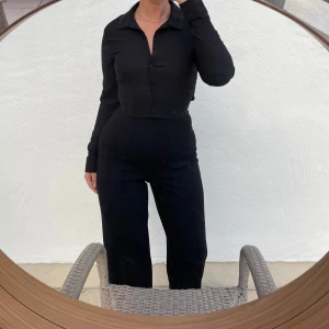 Svart byxdress med knappar - Säljer en stilren svart topp med knappar framtill. Den har en knytning i ryggen för extra detalj. Väldigt liten i storleken 