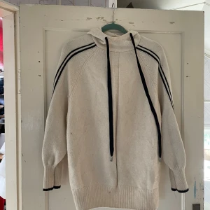 Vit stickad tröja från Pringle of Scotland x H&M - Säljer en superfin vit stickad tröja från Pringle of Scotland x H&M. Den har en cool design med svarta ränder längs ärmarna och en mysig polokrage med snörning. Perfekt för kyliga dagar när du vill vara både varm och stilren!