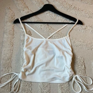 Vit linnetopp från Gina Tricot - Säljer en superfin vit linnetopp från Gina Tricot i storlek S. Toppen har smala axelband som korsas i ryggen och snygga knytband på sidorna för en justerbar passform. Perfekt för sommardagar eller en utekväll! 💫