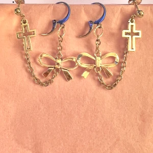 Örhängen med kors och rosett - Coola silvriga örhängen, gjorda av mig, i rostfritt stål. Är som 2 örhängen i ett så man måste ha 2 hål på örat🩶