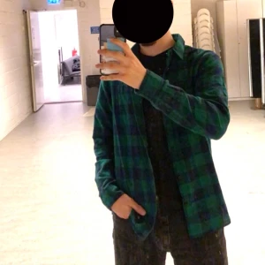 Grön och svart rutig skjorta - Säljer en snygg grön och svart rutig skjorta med långa ärmar. Perfekt för en avslappnad stil, kanske över en t-shirt eller som den är. Skjortan har en klassisk krage och knappar hela vägen ner. Den är i bra skick och passar perfekt för sommar, vinter