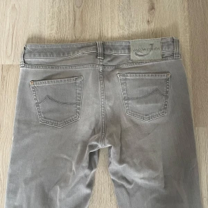 Grå jeans från Jacob Cohen - Säljer ett par snygga grå jeans från Jacob Cohen. De har en klassisk femficksdesign och en dragkedja med knappstängning. Jeansen är i en stilren grå färg och är i bra skick. Perfekta för både vardag och lite mer uppklädda tillfällen!