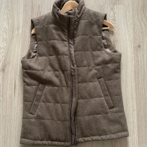 Brun quiltad väst - Säljer en snygg brun quiltad väst med dragkedja, från John henric. Perfekt för höst och vår, den har en stilren design med två fickor fram. Insidan är fodrad för extra komfort. Passar till både vardag och lite mer uppklädda tillfällen. Passar 175-185