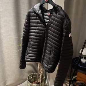 Svart dunjacka med huva - Säljer en snygg och varm colmar. svart dunjacka med huva. Jackan har en dragkedja framtill och är perfekt för kyliga dagar. Den är i bra skick och passar både till vardags och lite mer uppklädda tillfällen.