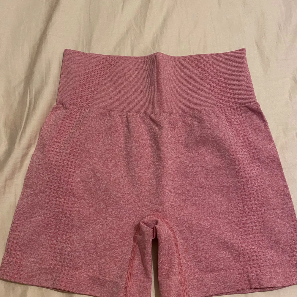 Säljer ett par snygga rosa shorts med hög midja. De är perfekta för träning och har en bekväm passform. Materialet är stretchigt och andas bra, vilket gör dem idealiska för intensiva träningspass. De har en ribbad detalj vid midjan som ger extra stöd.. Sportswear.