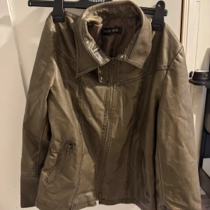 Brun skinnjacka från Hezvana - Säljer en snygg brun skinnjacka från Hezvana. Den har en klassisk krage och dragkedja framtill. Jackan har långa ärmar och två fickor med dragkedja. Perfekt för höst och vår!