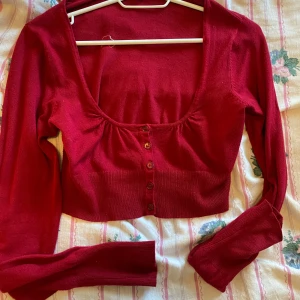 Röd croppad kofta - Säljer en superfin röd croppad kofta med knappar framtill. Den är perfekt för höst och vår, och har långa ärmar som håller dig varm. Materialet känns mjukt och skönt mot huden. Passar perfekt till både jeans och kjol. Hör av dig om du är intresserad! ❤️
