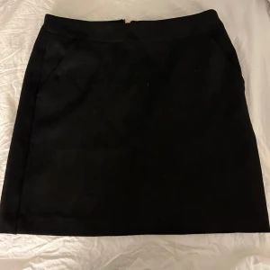 Svart kjol från Vero Moda - Säljer en svart kjol från Vero Moda i storlek XS. Kjolen har en dragkedja bak och två fickor fram och är perfekt för både vardag och fest. Den är i ett klassiskt snitt som gör den lätt att matcha med olika toppar och accessoarer.