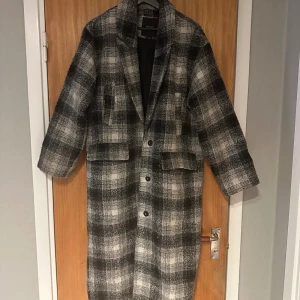 Rutig kappa från Monki - Säljer en superfin rutig kappa från Monki i storlek XS. Den har en klassisk svart och grå färgkombination med ett stilrent rutmönster. Kappan är långärmad och perfekt för höst och vinter. Den har knappar framtill och en skön passform som är både snygg och bekväm. Perfekt för att hålla sig varm och trendig!