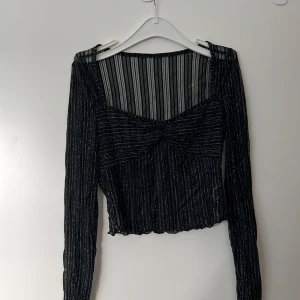 Svart glittrig topp - Säljer en superfin svart glittrig topp med lång ärm. Den är croppad och har en snygg ribbad design. Perfekt för festliga tillfällen med sin glittriga look och transparenta detaljer.