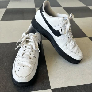 Vita Nike Air Force med Svart sula - Vita air force med svart sula samt swoosh logga. Använda ett fåtal gånger vilket ändå har lett till att de är aningens creasade. Utöver det är de i fint skick.