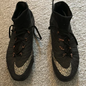 Svarta fotbollsskor från Nike - Säljer ett par svarta hypervenoms som inte säljs längre. Skorna har en hög strumpa för extra stöd och snörning framtill. Perfekta för fotbollsträning eller match! Skriv om ni har några fler frågor😁