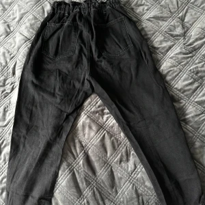 Svarta byxor från Zara - Paperbag straight jeans från Zara i storlek 40 i mycket fint skick. Byxorna har en hög midja med resår och knappar framtill. De är tillverkade i ett mjukt material och har en avslappnad passform med raka ben. 