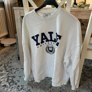 Vit sweatshirt från Pull&Bear med Yale-tryck - Säljer en snygg vit sweatshirt från Pull&Bear med ett stort Yale University-tryck i mörkblått på framsidan. Tröjan är perfekt för en avslappnad stil och har långa ärmar. Den är i bra men använt skick och passar perfekt för höst och vår.