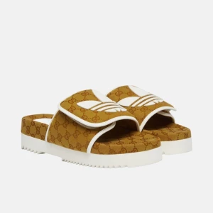 Bruna sandaler med vit logga - Snygga bruna Gucci X Adidas sandaler. De har en cool mönstrad design och en bekväm vit sula. Perfekta för sommaren och att glida runt i stan med stil!
