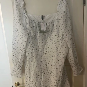 Ny Vit blommig klänning - Säljer en superfin vit klänning med små blå blommor. Den har långa ärmar och en dragkedja på sidan för enkel påklädning. P🌸