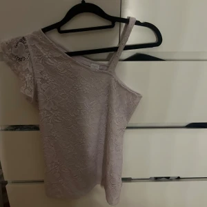 Vit spets topp - Säljer en superfin vit spets topp med en unik design. Den är offshoulder med en axelbandslös stil på ena sidan och en kort ärm med spetsdetaljer på andra sidan. Perfekt för sommarens fester eller en utekväll! storlek 170 men går på mig som har L så skulle säga XS/M